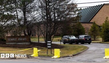 view of the Temple Israel sign out front of the synagogue, with police cars and yellow tape in view