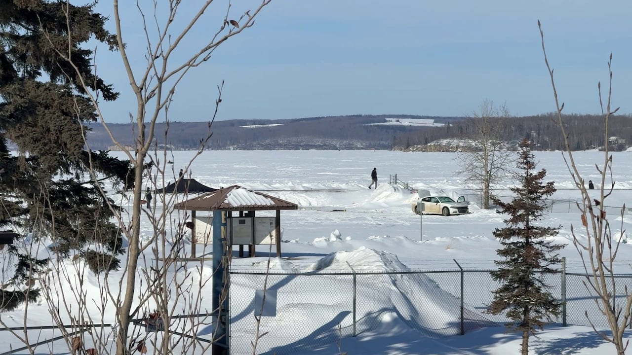 A car is parked near a frozen shoreline at a boat ramp