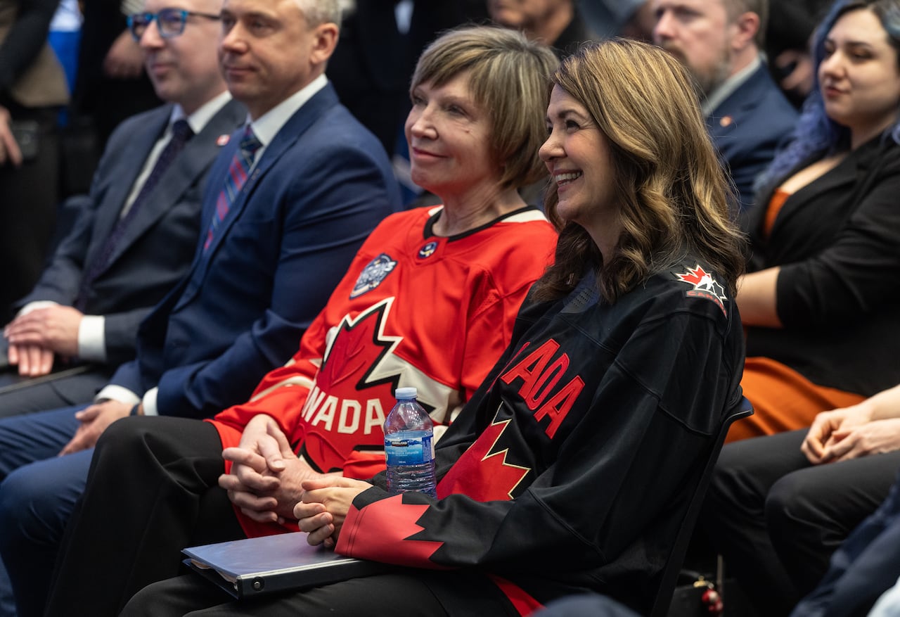 Two women sit in a crowd and listen to a speech.