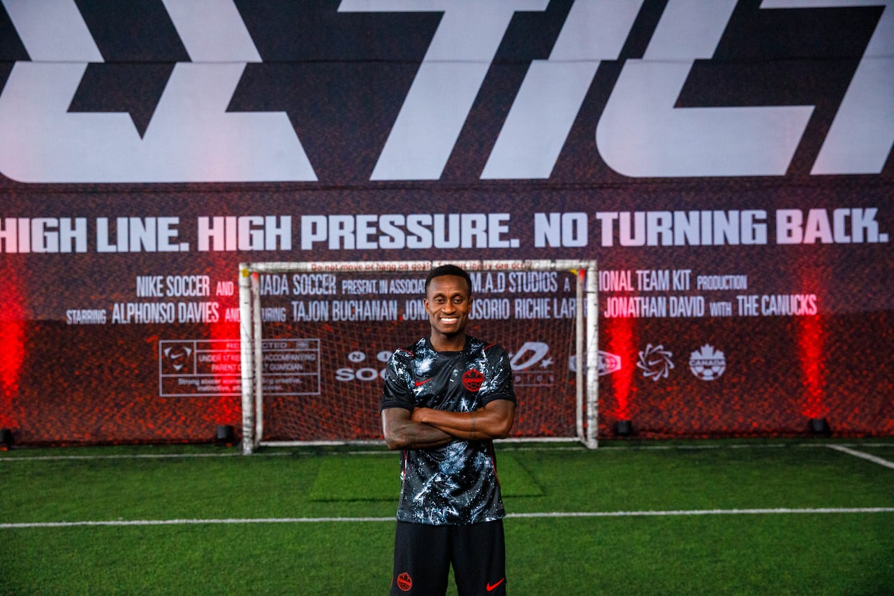 Man wearing a black soccer jersey stands in front of soccer net