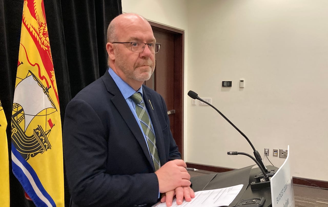 Bald man with glasses, wearing a suit, stands at a podium in front of a microphone. 