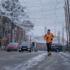 A man jogs in the street beneath nylon netting strung over the road. 