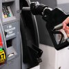 A person's hand grips a gas pump nozzle at a gas station. A digital display on the gas pump says regular gas is $5.29.