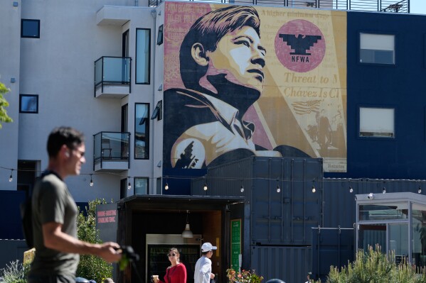 Pedestrians walk below an image of César Chavez on a mural in San Francisco, Wednesday, March 18, 2026. (AP Photo/Jeff Chiu)