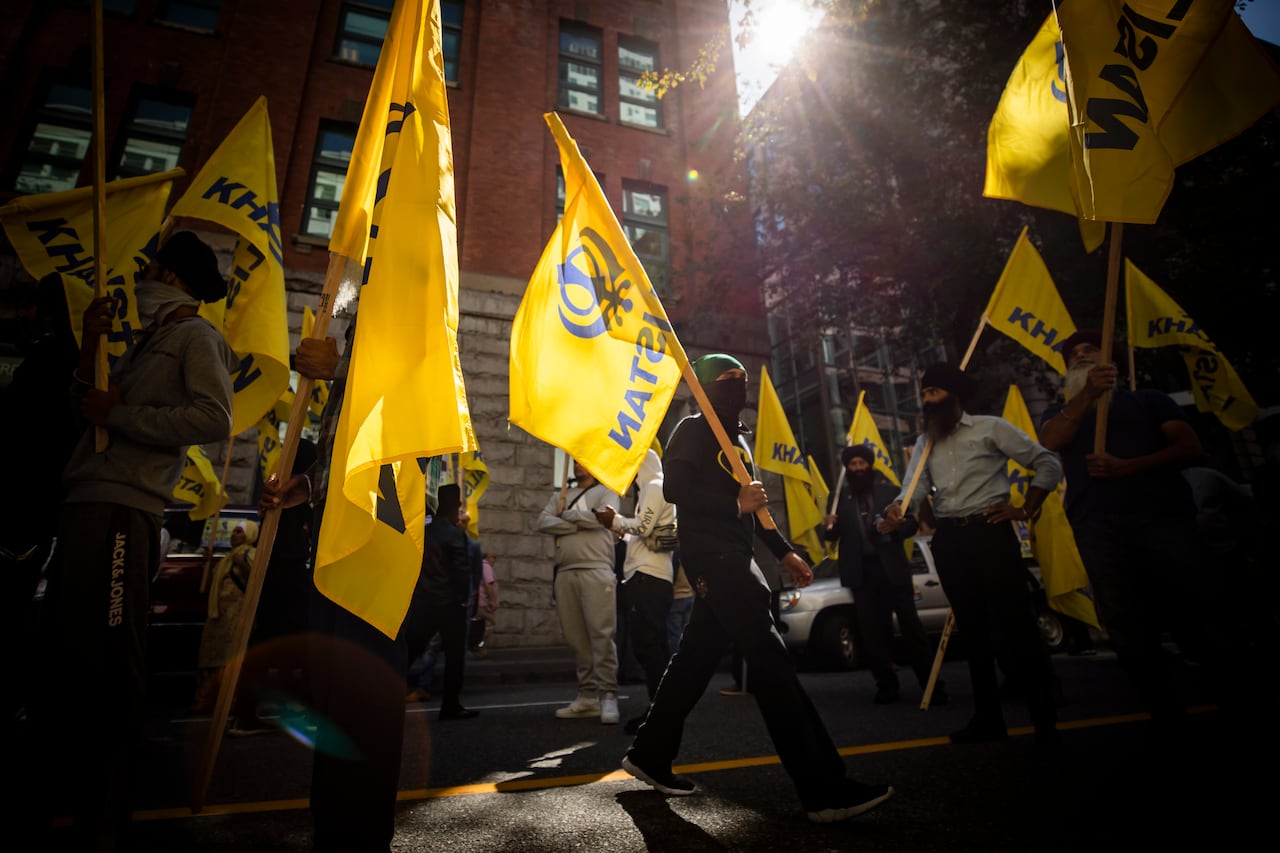 People carrying yellow flags walk down a city street on a sunny day.