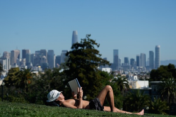 Clive Lovejoy reads a book while lying on grass at Dolores Park in San Francisco, Wednesday, March 18, 2026. (AP Photo/Jeff Chiu)