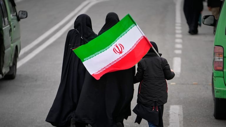 Two women and a child holding an Iranian flag walk...