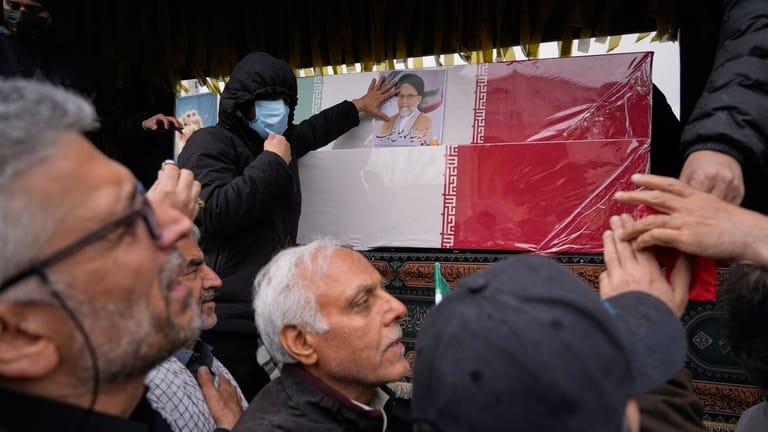 Iranians reach toward the coffins as they follow the funeral...