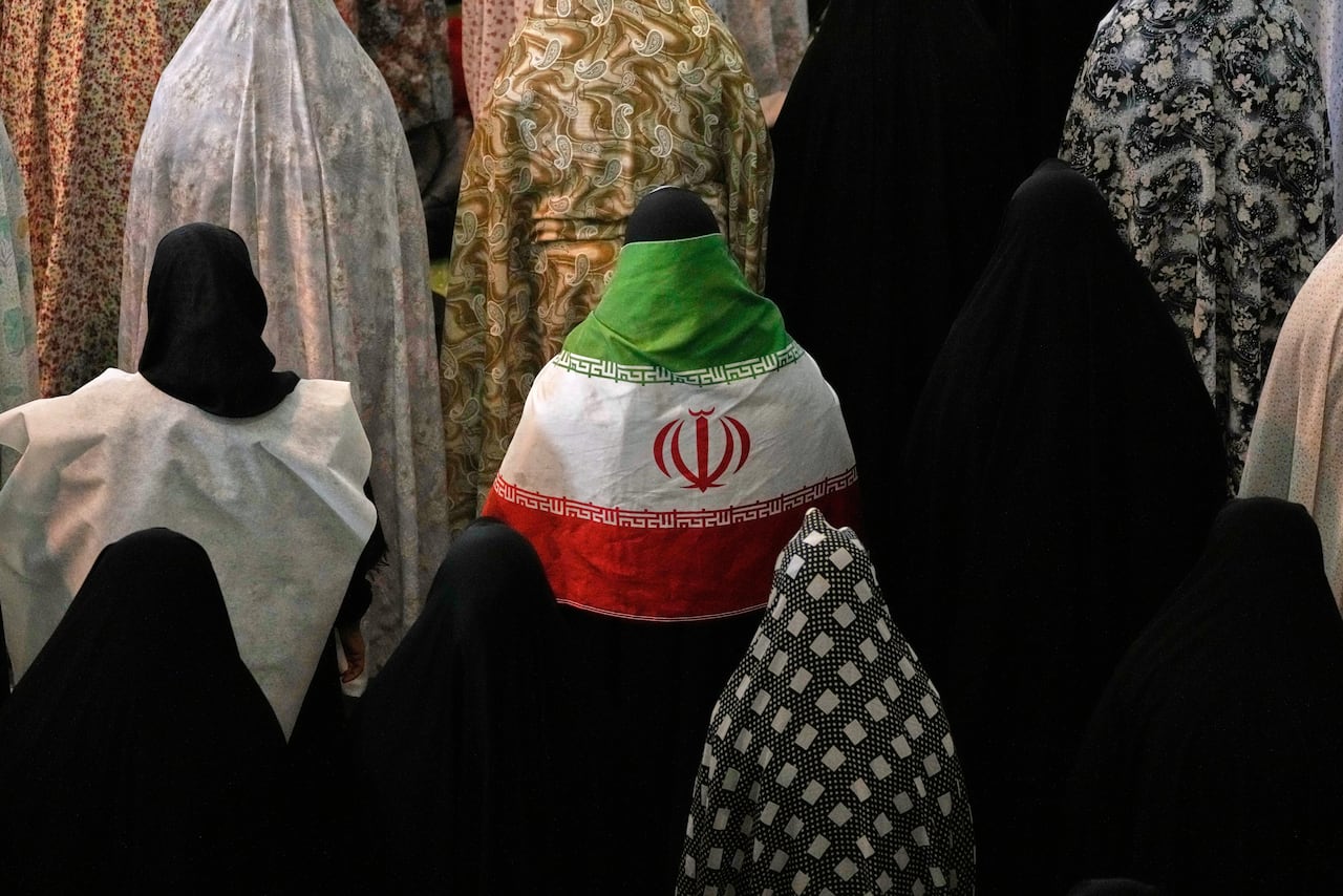 Iranian worshippers pray in a large crowd.