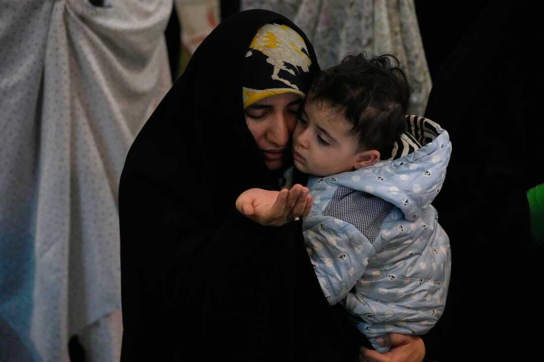 An Iranian worshipper prays during a ceremony to perform Eid al-Fitr prayers marking the end of the holy fasting month of Ramadan while holding a child at the Imam Khomeini Grand Mosque in Tehran, Iran, Saturday, March 21, 2026.