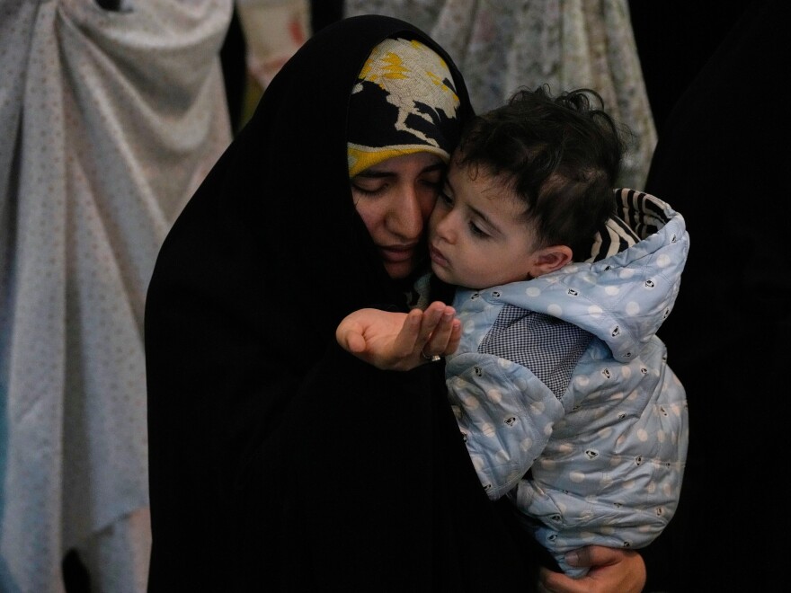 An Iranian worshipper prays during a ceremony to perform Eid al-Fitr prayers marking the end of the holy fasting month of Ramadan while holding a child at the Imam Khomeini Grand Mosque in Tehran, Iran, Saturday, March 21, 2026.