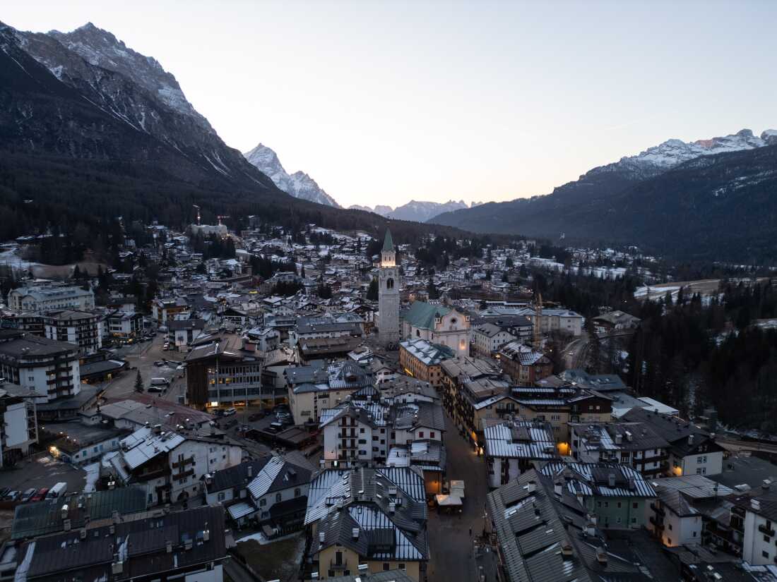 The illuminated bell tower of the Basilica Minore dei Santi Filippo e Giacomo stands at the heart of Cortina d’Ampezzo as evening settles over the valley. 