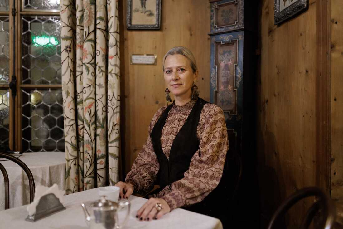 Servane Giol sits in a wood-paneled room beside an 18th-century painted pendulum clock.