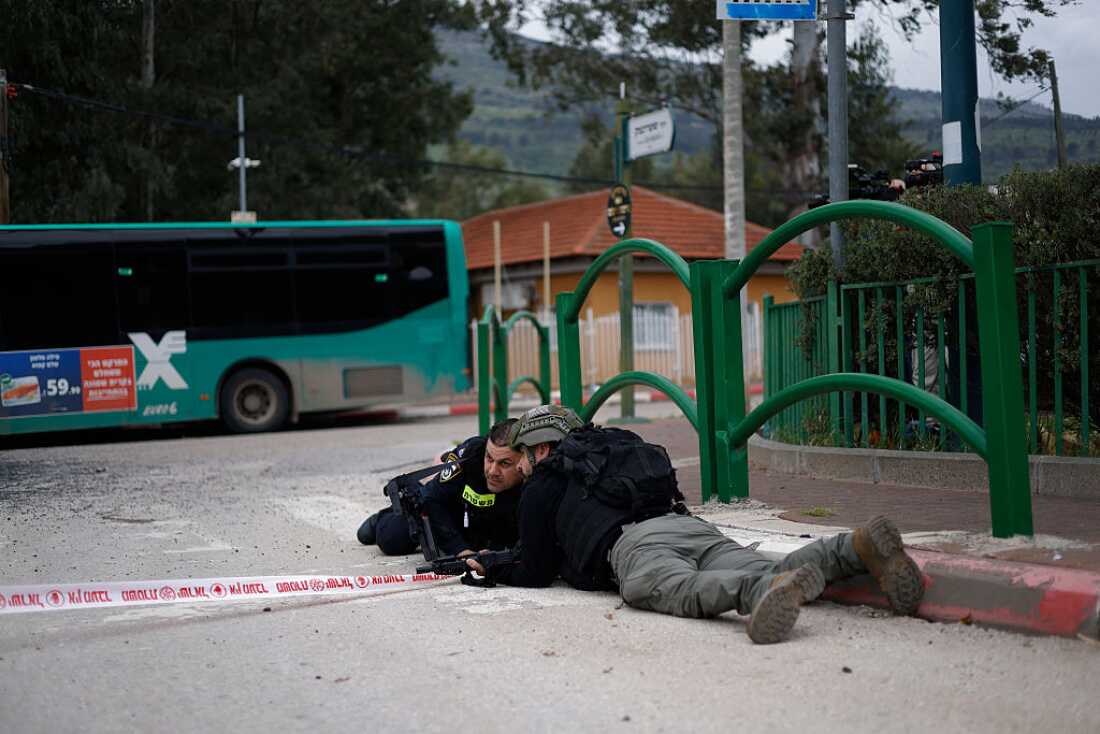 Israeli security forces take cover during a siren alert while gathering at the site of a Hezbollah missile strike that targeted a bus in the northern Israeli border town of Kiryat Shmona on March 23, 2026.