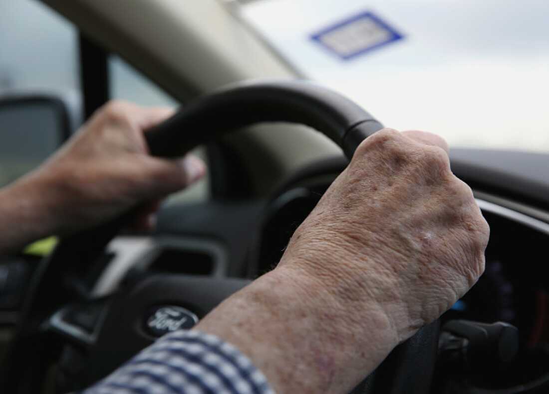 This photo shows the hands of an older driver gripping a steering wheel in a car.