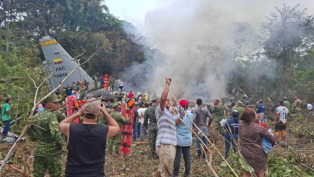 People stand around a military cargo plane that crashed after taking off from Puerto Leguizamo, Colombia, a remote municipality in the Amazonian province of Putumayo, Monday, March 23, 2026.