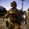 Federal enforcement officers wearing camouflage uniforms and carrying firearms stand guard on a street near an Immigration and Customs Enforcement facility in Portland, Oregon, on October 6, 2025.