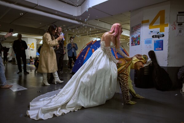 A woman dressed as a bride rides on the back of a man dressed as a turtle during a singles event in an underground parking garage used as a shelter against possible Iranian missile attacks in Tel Aviv, Israel, Tuesday, March 17, 2026. (AP Photo/Oded Balilty)