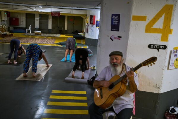 A man plays the guitar as people attend a yoga class in an underground parking garage used as a shelter against possible Iranian missile attacks in Tel Aviv, Israel, Tuesday, March 17, 2026. (AP Photo/Oded Balilty)