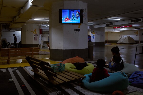 Children watch TV in an underground parking garage where people spend the night as a precaution against possible Iranian missile attacks in Tel Aviv, Israel, Thursday, March 12, 2026. (AP Photo/Oded Balilty)