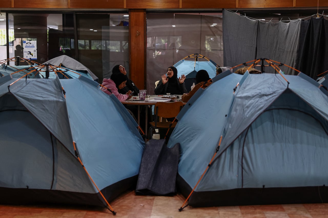 Women sit around a table in a school next to tents.