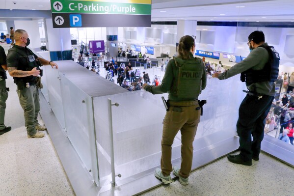 Federal immigration agents peer over railings on the floor above the lines of air travelers progressing to the TSA security checkpoint in Terminal C at the George Bush Intercontinental Airport, Monday, March 23, 2026, in Houston. (AP Photo/Michael Wyke)
