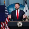 Vice President JD Vance speaks at a podium next to a sign that says "White House Press Briefing, Wednesday, October 1, 2025." An American flag is behind him and the presidential seal is on the podium.