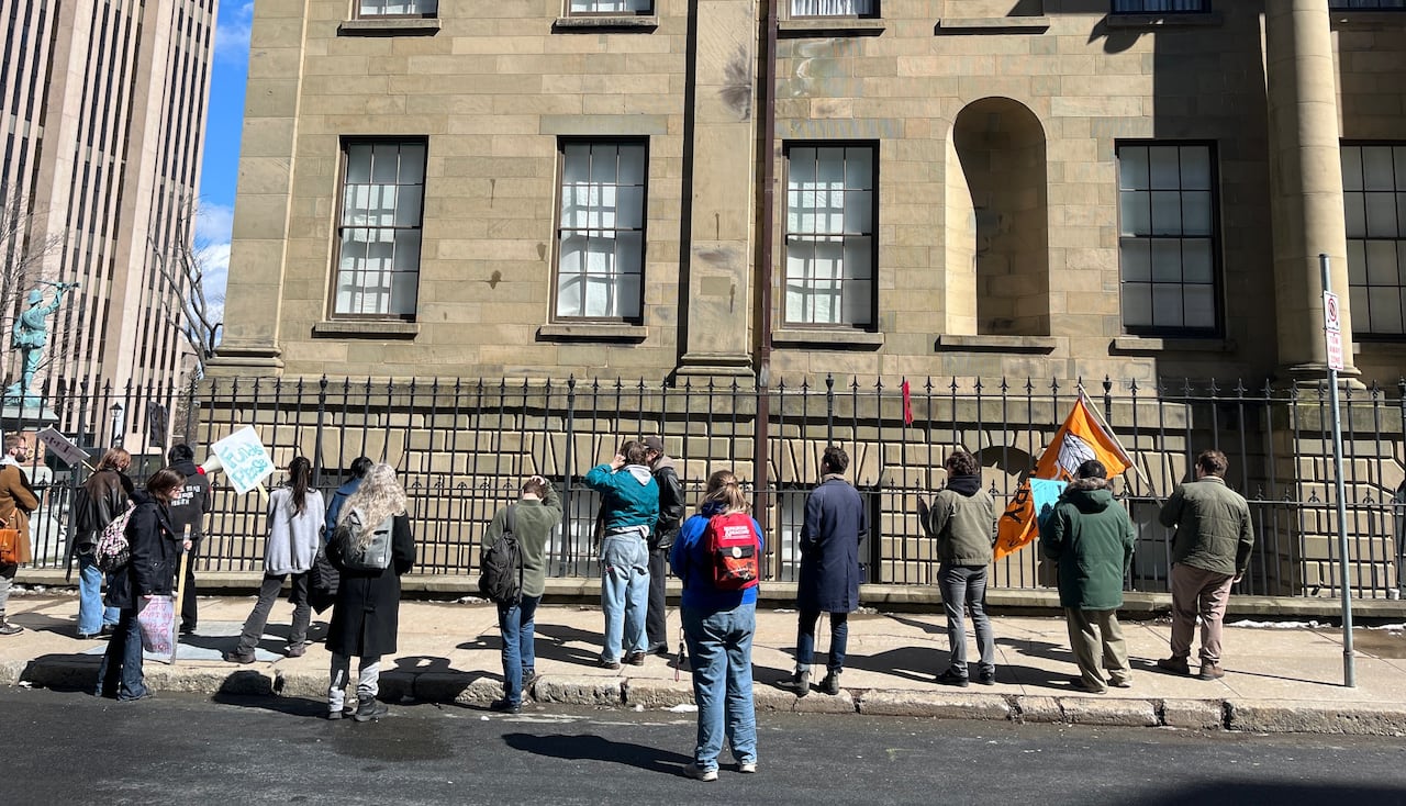 A group of people, some holding signs, stand outside a large building.