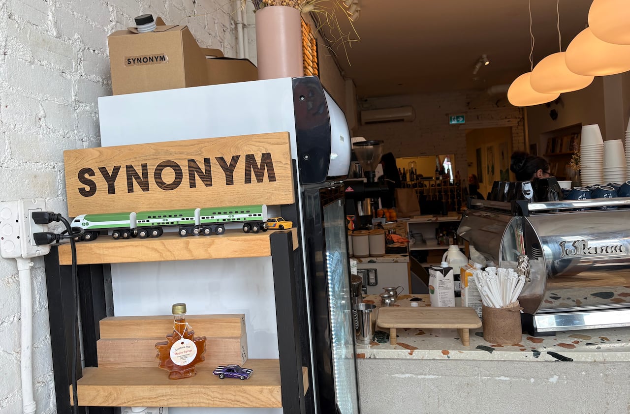 The interior of a cafe with a wooden shelf featuring a model GO Train and the word "Synonym."