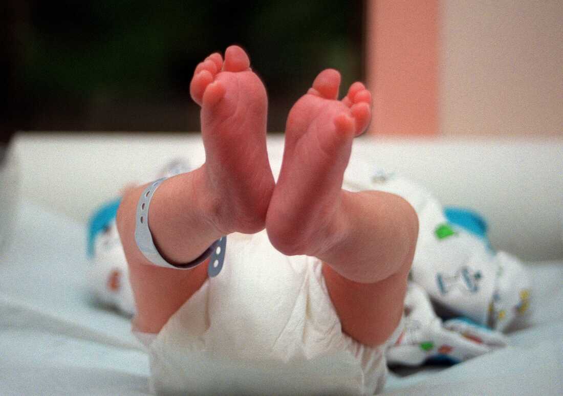 A newborn baby's feet are shown in a close-up photo.  A hospital anklet is visible. 
