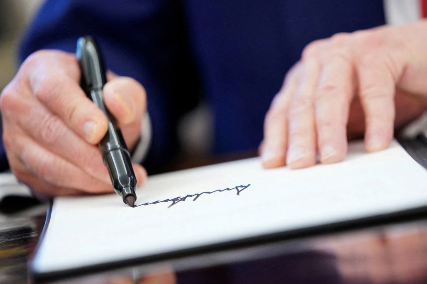 President Trump writes his signature as he signs executive orders and proclamations in the Oval Office in 2025.