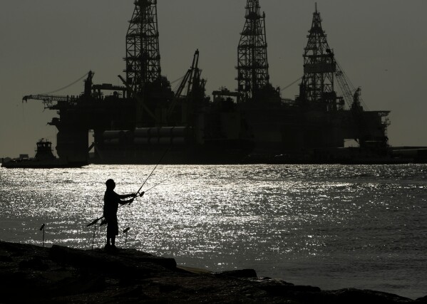 A man fishes near docked oil drilling platforms May 8, 2020, in Port Aransas, Texas. (AP Photo/Eric Gay, File)
