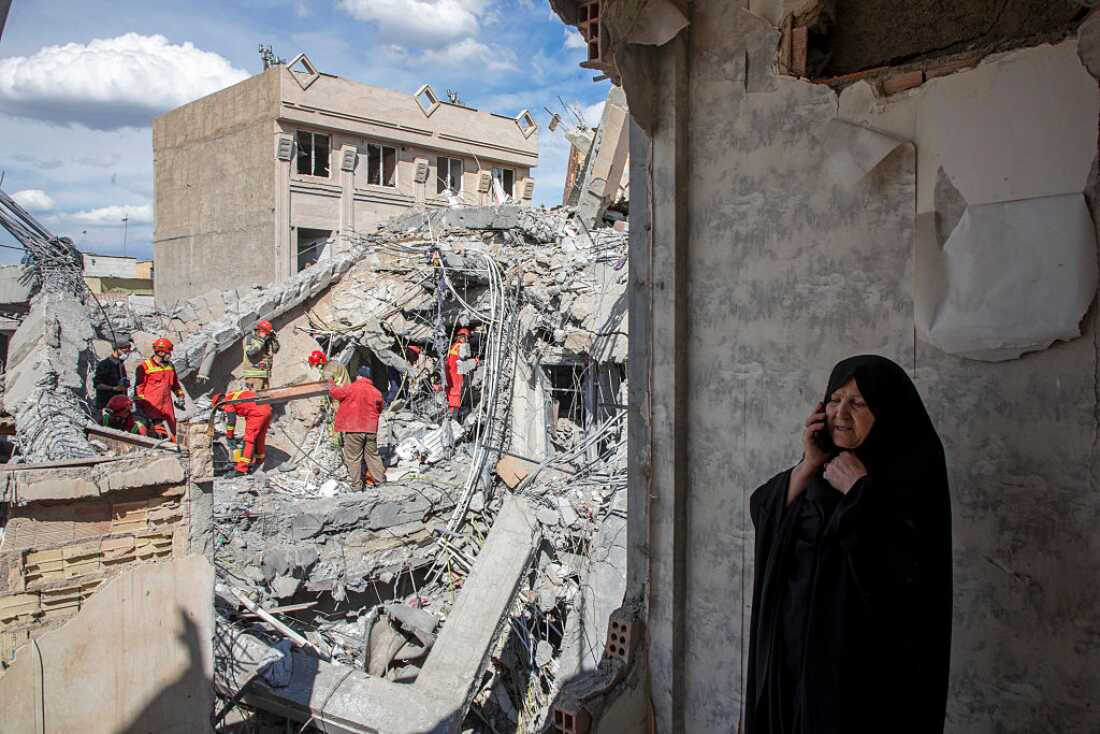 A woman speaks on the phone as emergency workers sift through rubble of a residential building that was hit in an airstrike in the early hours of March 27, 2026 in Tehran, Iran.