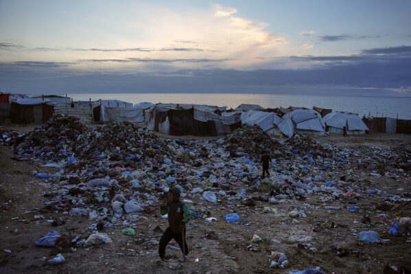 Children walk over a pile of garbage at a makeshift tent camp for displaced Palestinians on a beach in Deir al-Balah, in the Gaza Strip Friday, Jan. 16, 2026. (AP Photo/Abdel Kareem Hana)