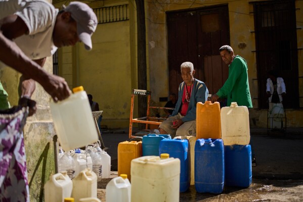 A man fill containers with potable water during a blackout in Havana, Sunday, March 22, 2026. (AP Photo/Ramon Espinosa)