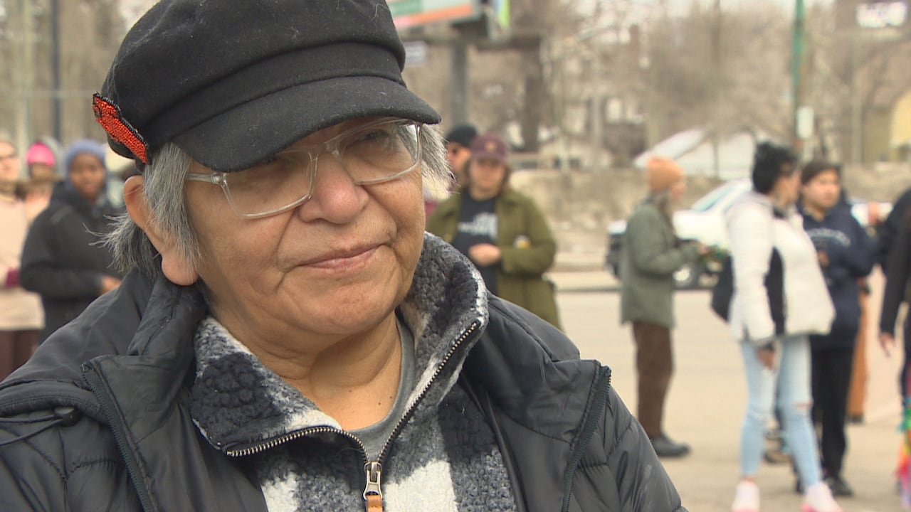 Woman with short grey hair wears a black hat with a beaded red dress pinned to the side.
