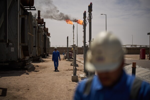 Workers walk in an area at a degassing station in Zubair oil field, whose operations have being reduced due to the Mideast war triggered by the U.S. and Israeli attacks on Iran, near Basra, Iraq, Saturday, March 28, 2026. (AP Photo/Leo Correa)
