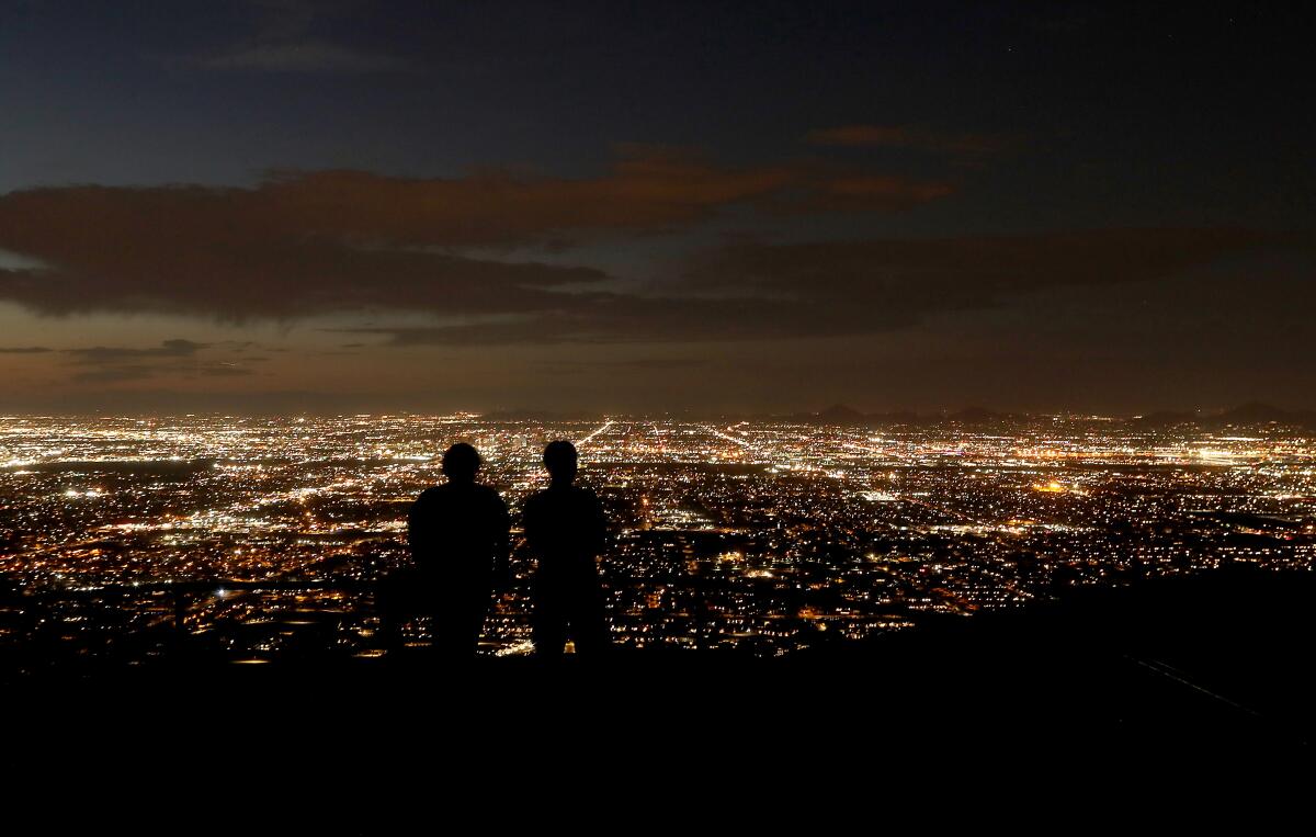 Two people in a high area look at a lighted city at night.