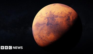 Artemis II sits in the Vehicle Assembly Building at NASA’s Kennedy Space Center as three workers wearing white hard hats look up at the rocket