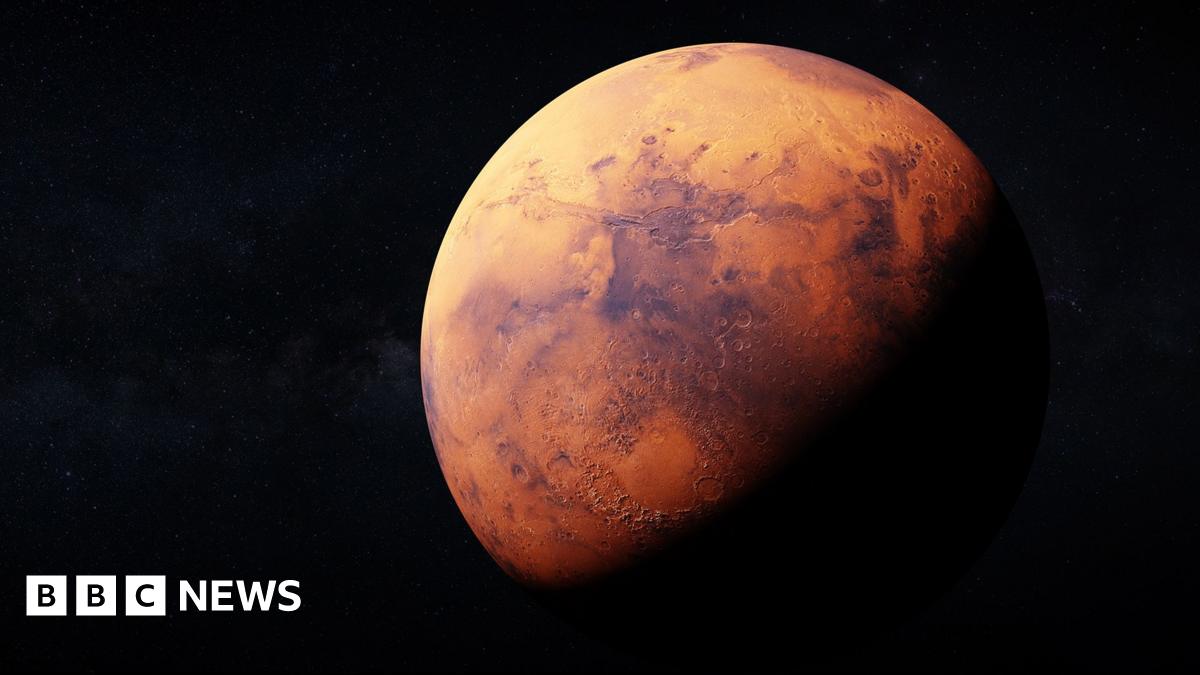 Artemis II sits in the Vehicle Assembly Building at NASA’s Kennedy Space Center as three workers wearing white hard hats look up at the rocket