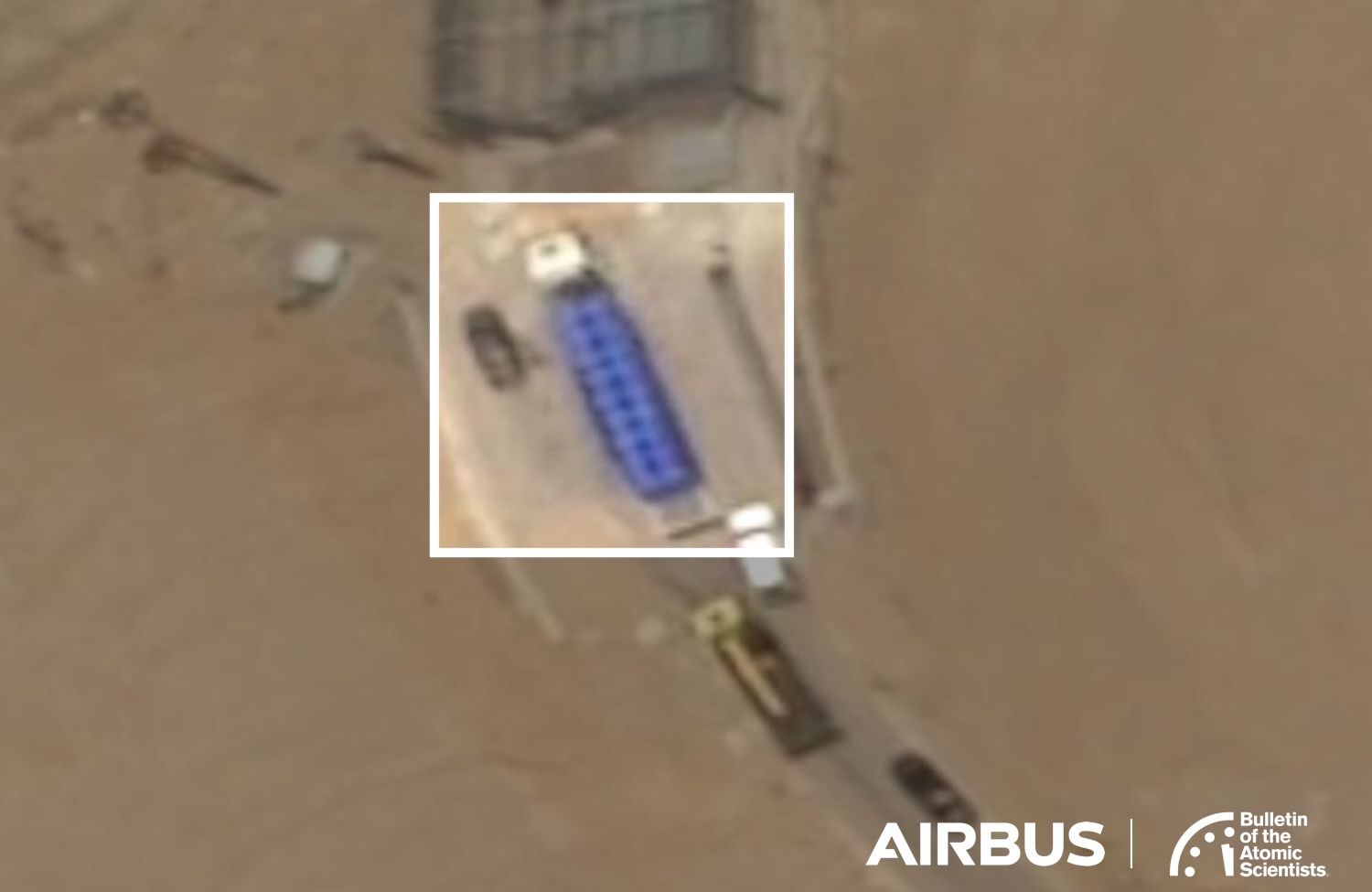 Satellite view of a tunnel entrance with a blue truck, several smaller vehicles, and surrounding sandy terrain.