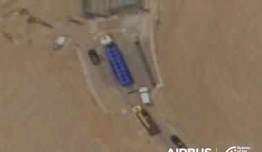 Satellite view of a tunnel entrance with a blue truck, several smaller vehicles, and surrounding sandy terrain.