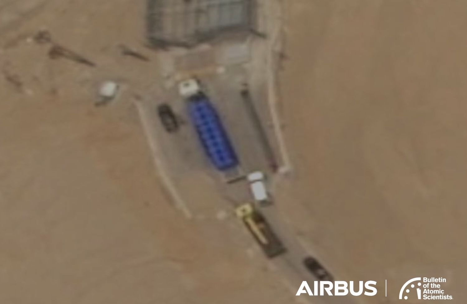Satellite view of a tunnel entrance with a blue truck, several smaller vehicles, and surrounding sandy terrain.