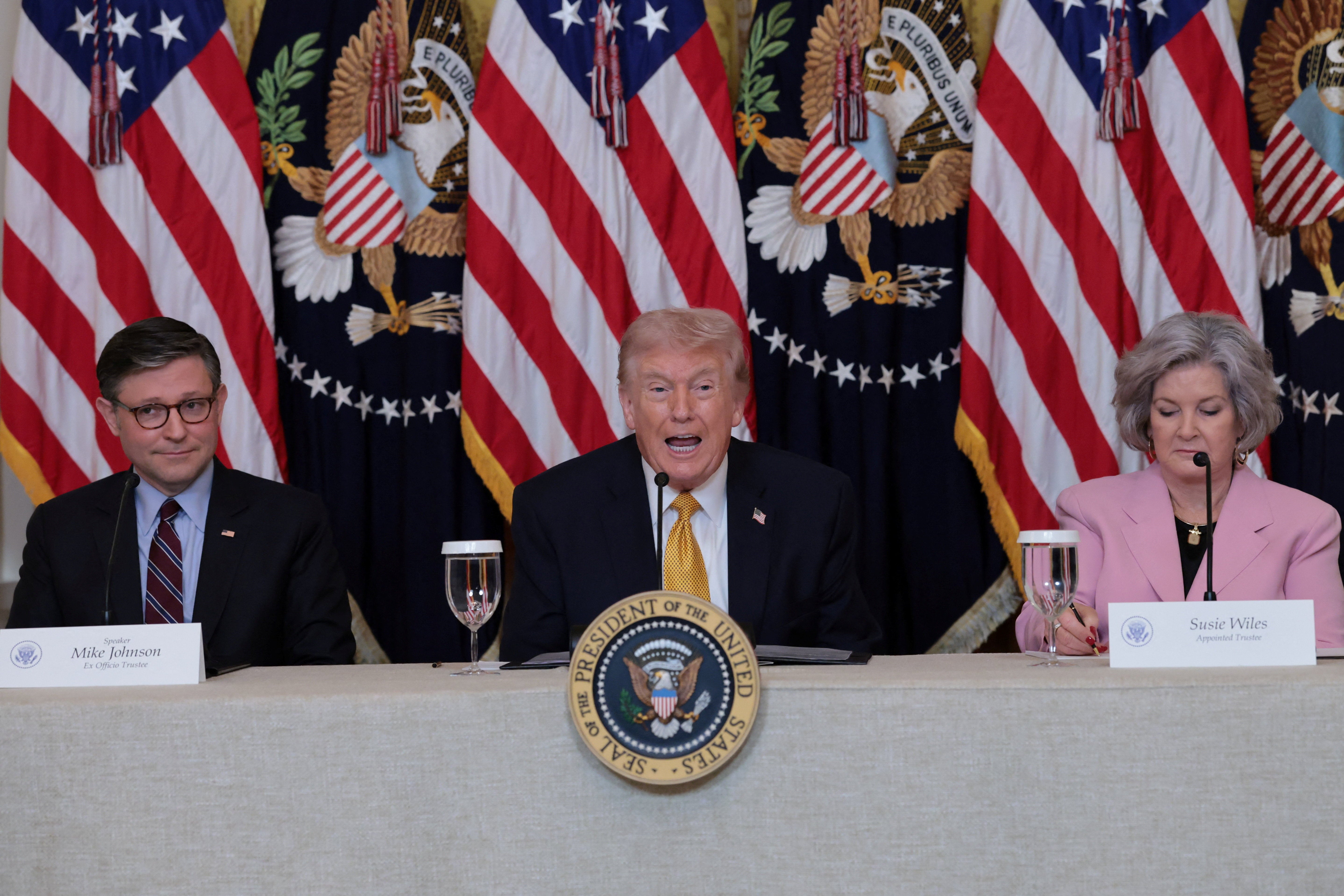 U.S. President Donald Trump, flanked by the Speaker of the House Mike Johnson (R-LA) and White House chief of staff Susie Wiles, speaks during a lunch with the Kennedy Center board members in the East Room of the White House in Washington, D.C., U.S., March 16, 2026. REUTERS/Jonathan Ernst
