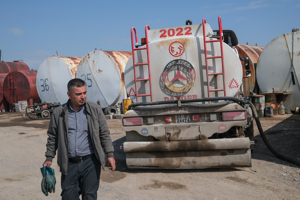 An oil worker in Erbil, Iraq, walks past a fuel truck and large storage tanks.