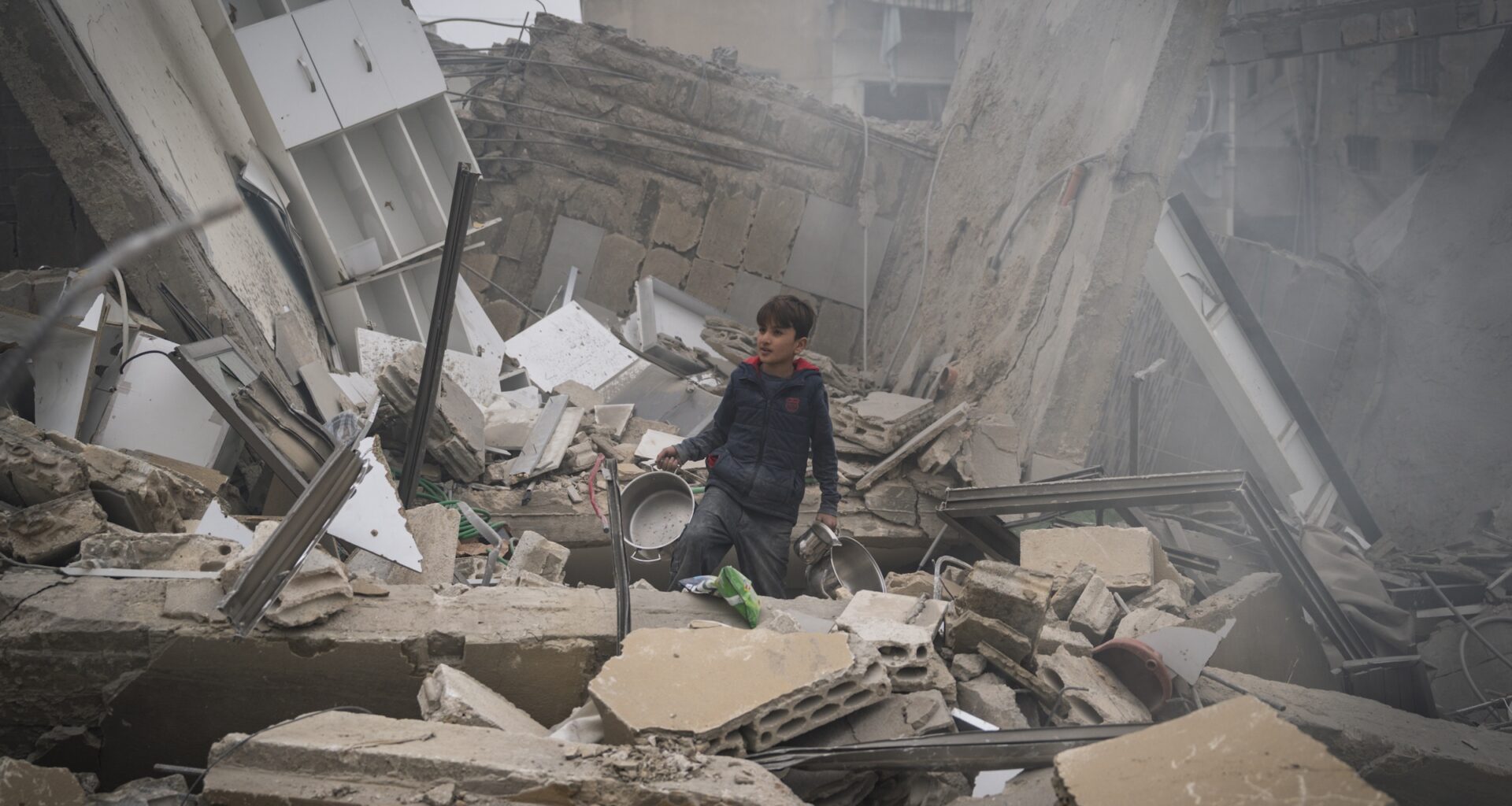 A child searches for kitchen tools inside of the debris of a building that has collapsed after an IDF airstrike on March 18, 2026 in Beirut, Lebanon.