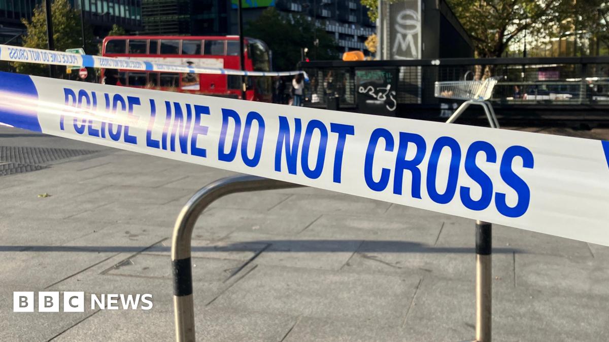 Blue and white police tape which reads 'police line do not cross'. A red London bus is in the background