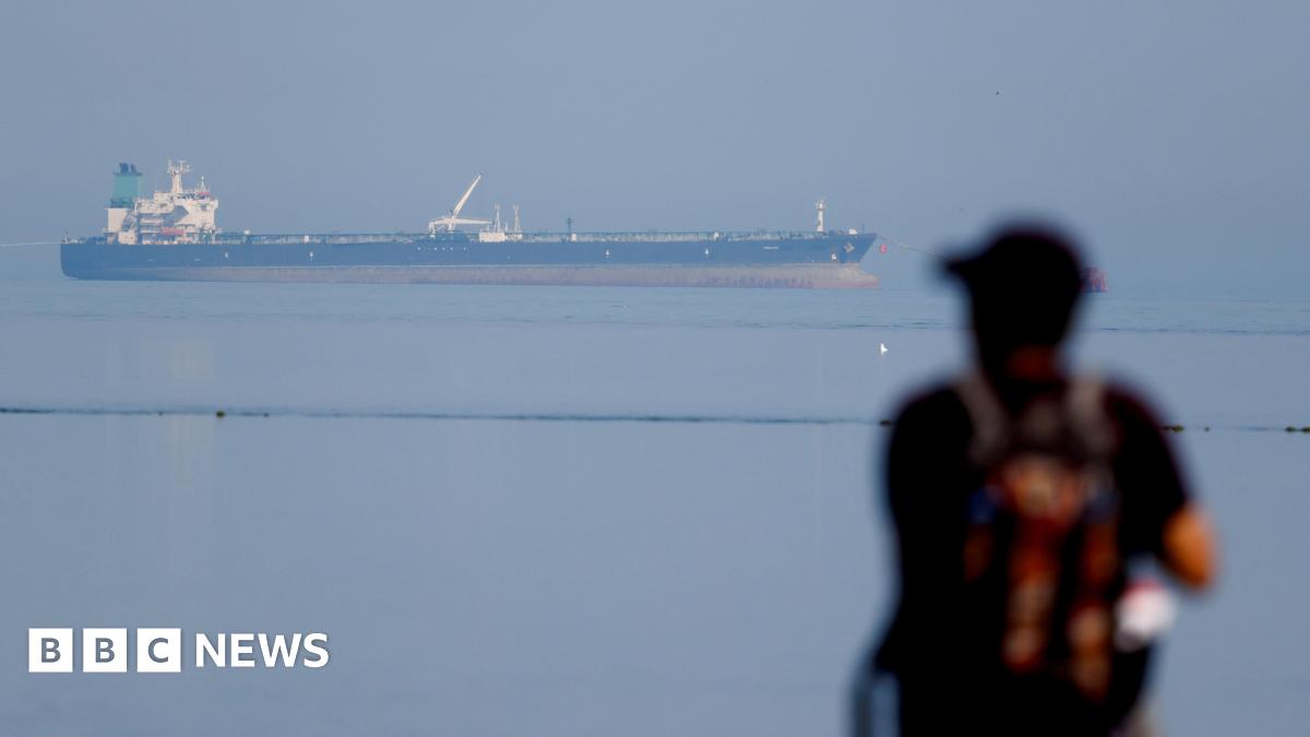 A woman with dark hair and a multiple colour jumper siting on a green sofa inside her living room.