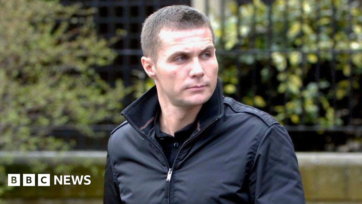 Steven Lyons has cropped brown hair and is wearing a black jacket with the collar turned up. He is looking off to the left with a serious expression on his face