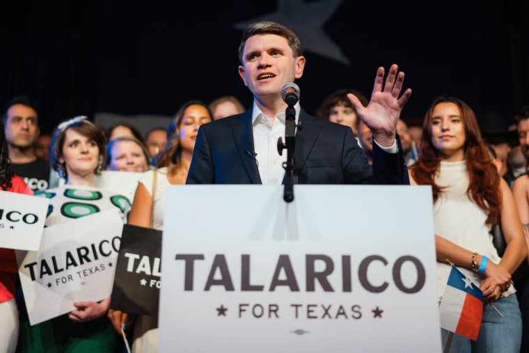 James Talarico speaks at a podium in front of people holding signs that say "Talarico for Texas"